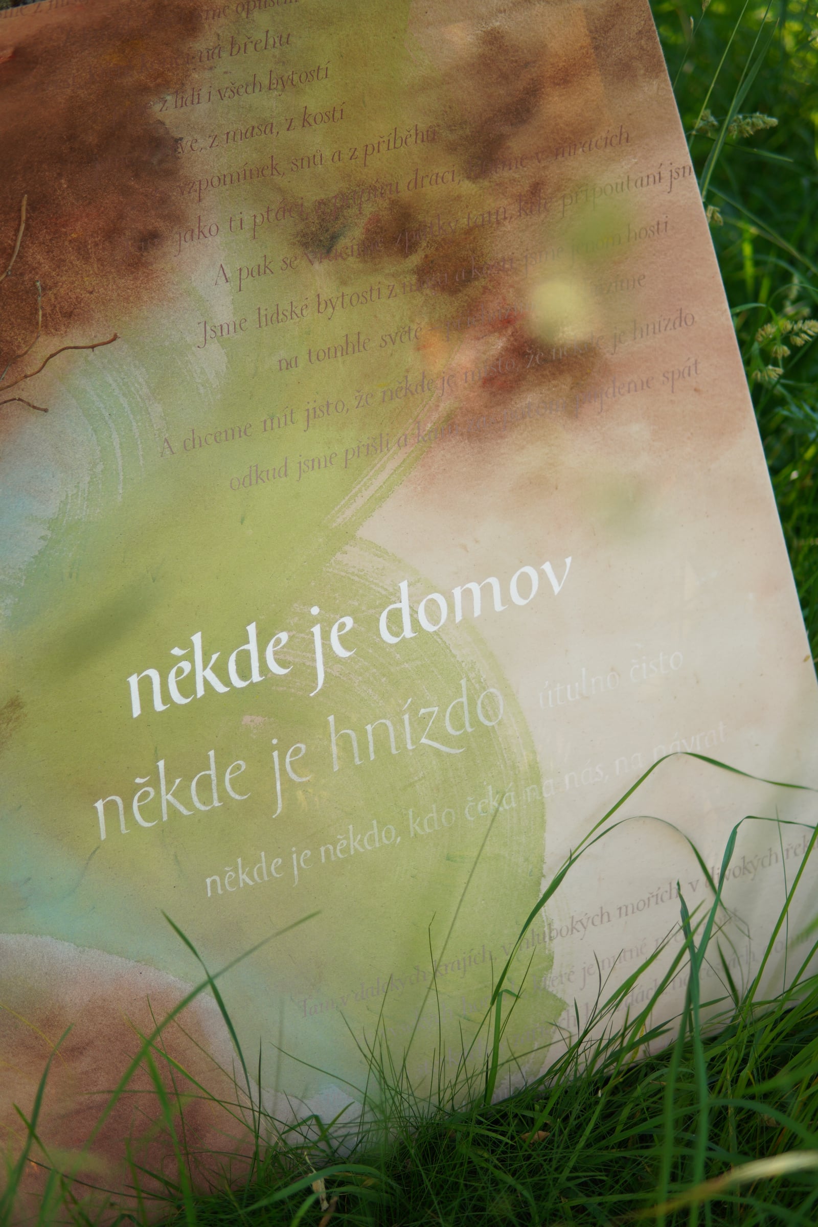 Detail nápisu na plátně mezi stébly trávy.