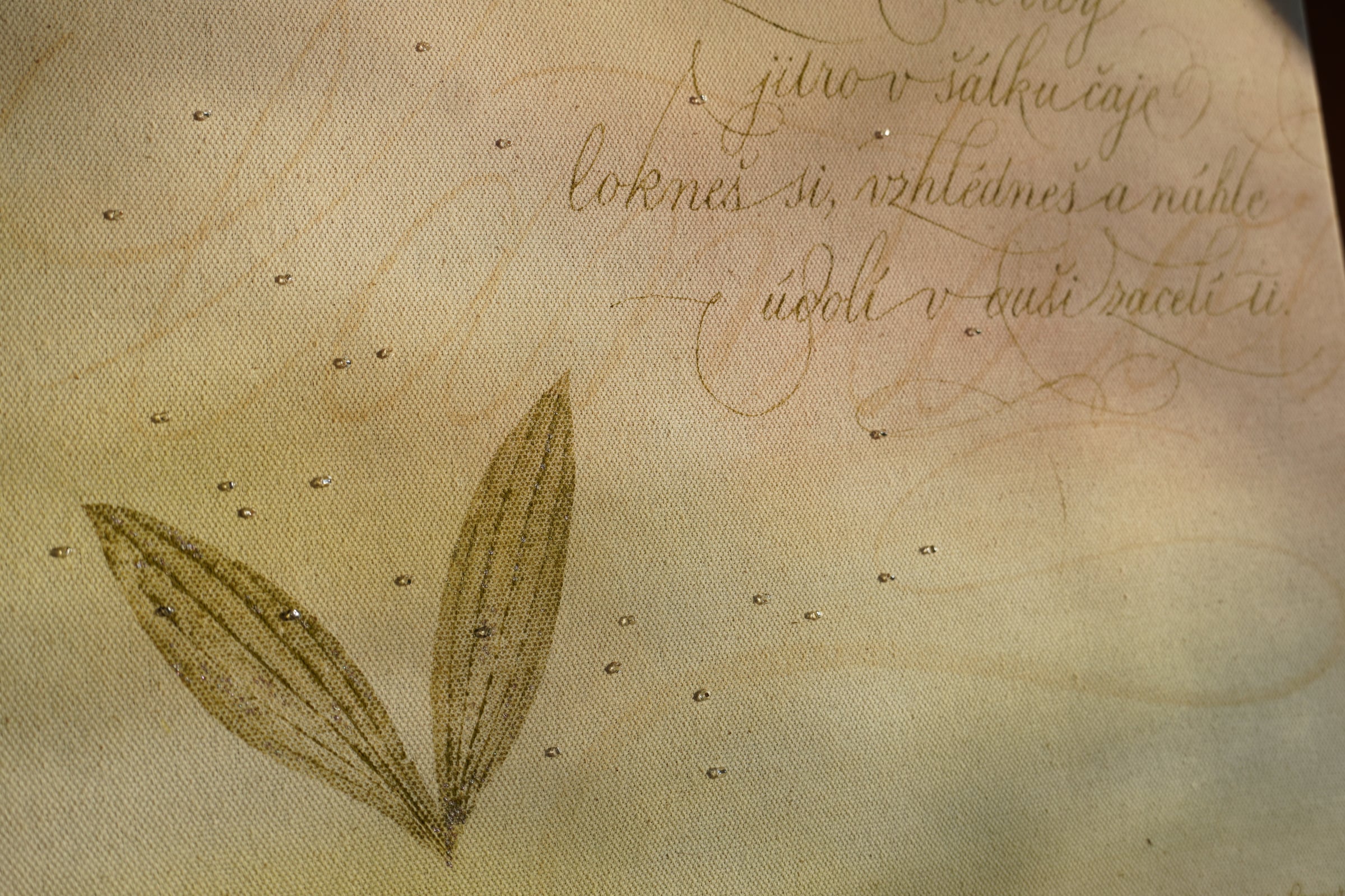 Detail textu, lístků jitrocele a drobných korálků na plátně.