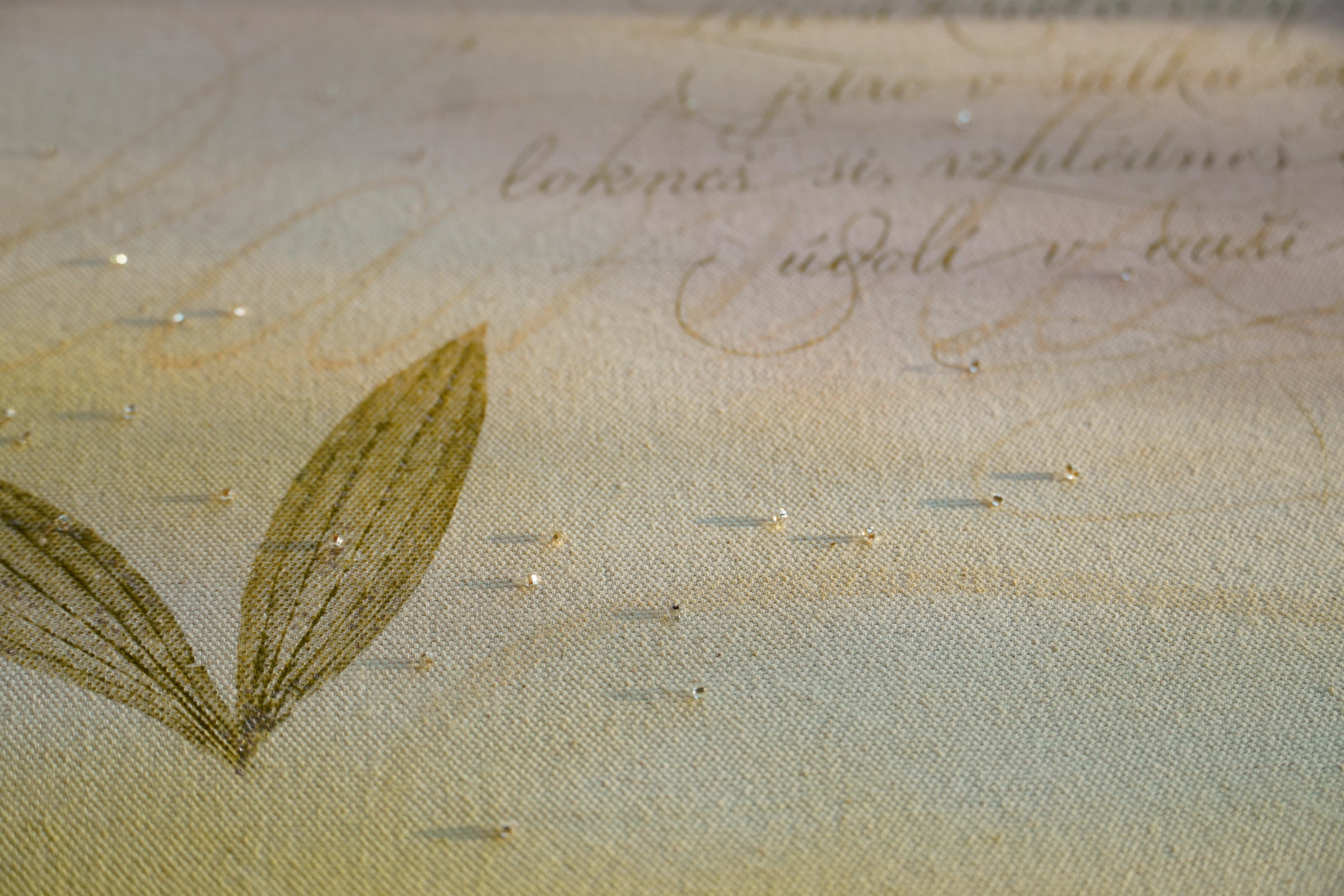 Detail lístků jitrocele a korálků na textuře plátna.