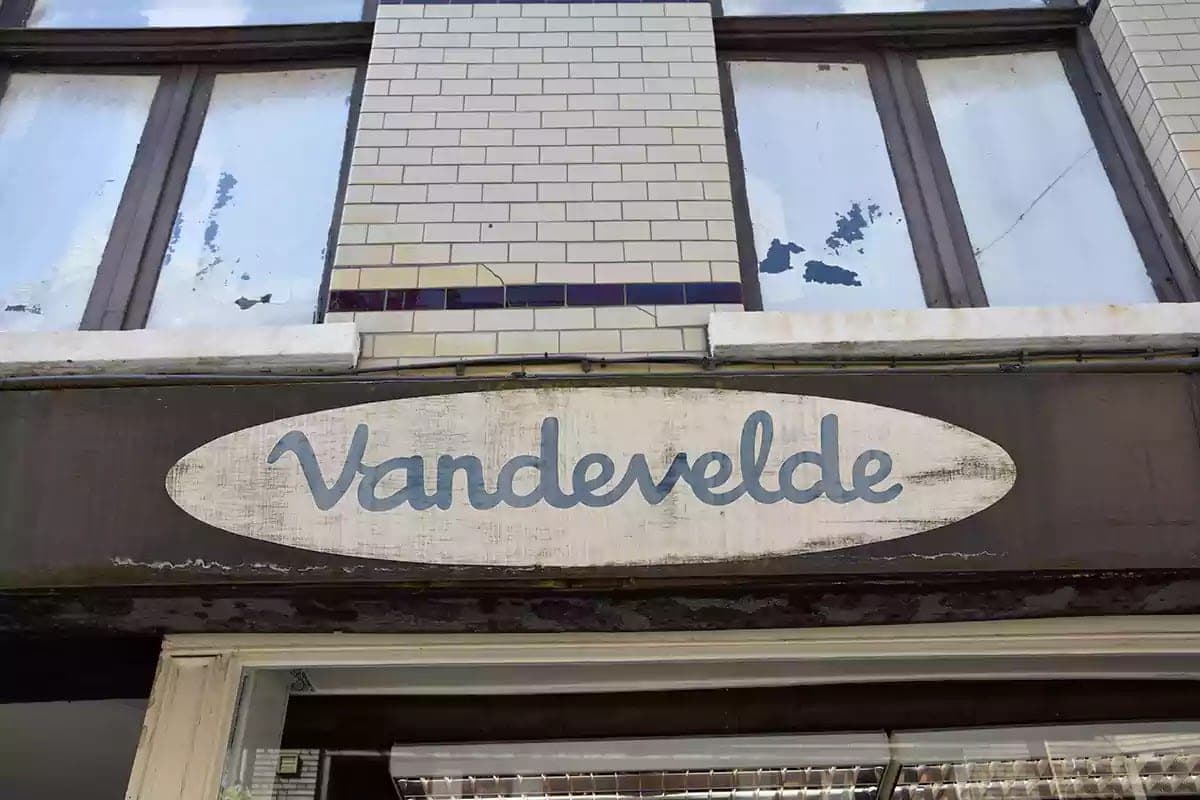 Oprýskaný oválný štít Vandevelde nad vchodem do obchodu
