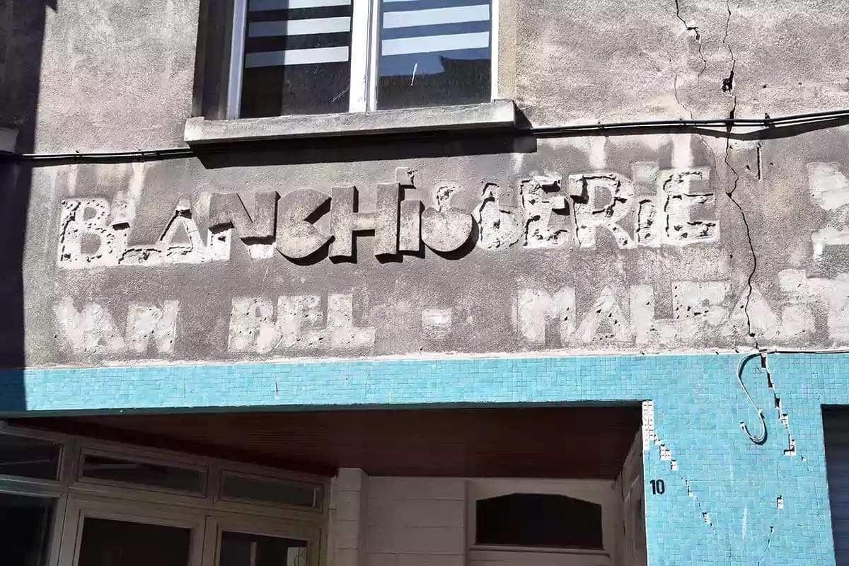 Oprýskaný plastický nápis Blanchisserie na staré fasádě