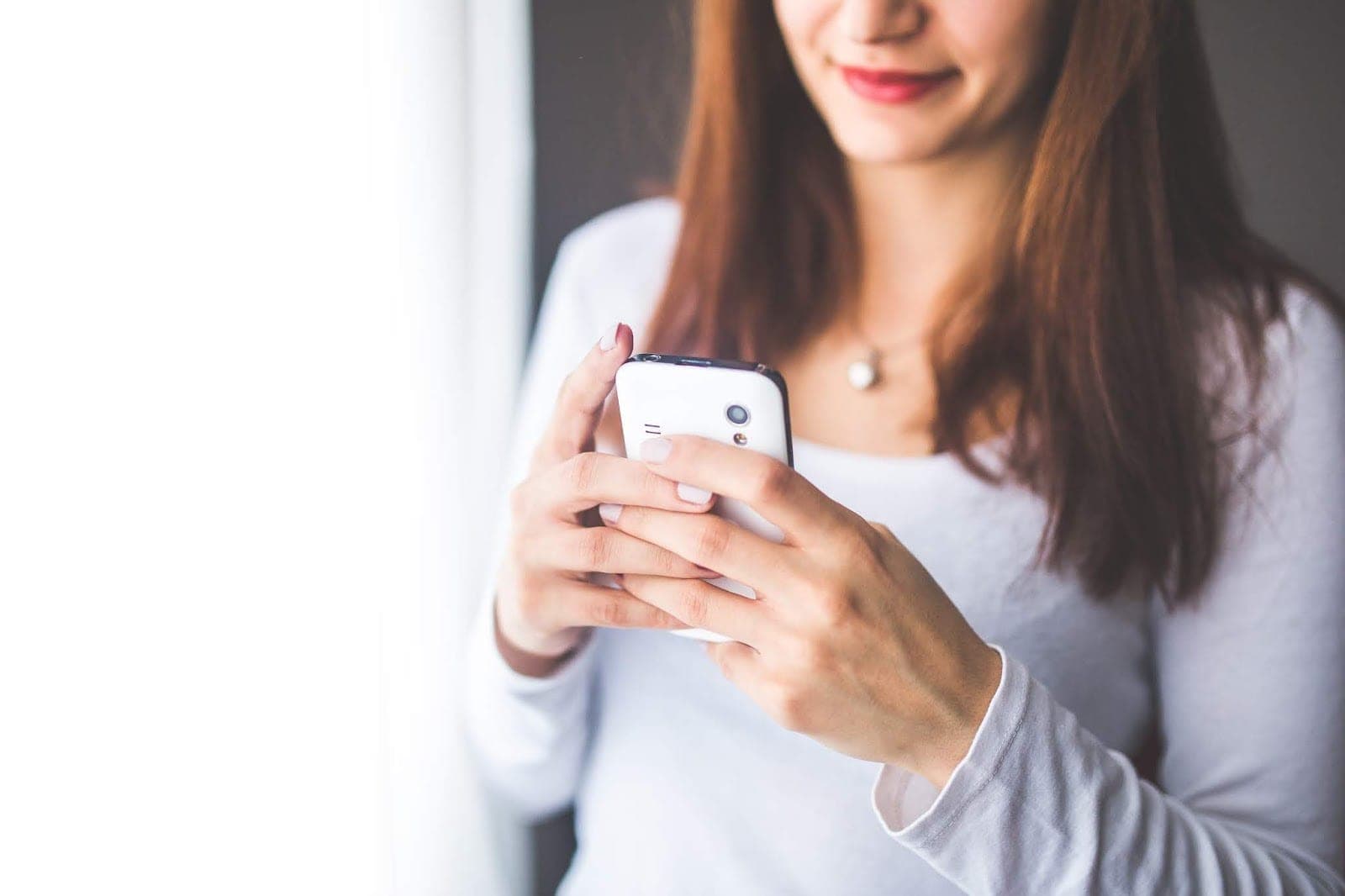 Dívka v bílém tričku se usmívá do mobilu